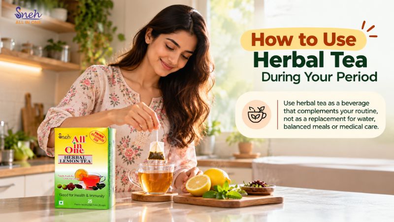 Smiling woman in a floral kurta dunking a tea bag into a glass cup in a bright kitchen, with lemons, mint, and a box of Sneh All in One Herbal Lemon Tea on the counter.